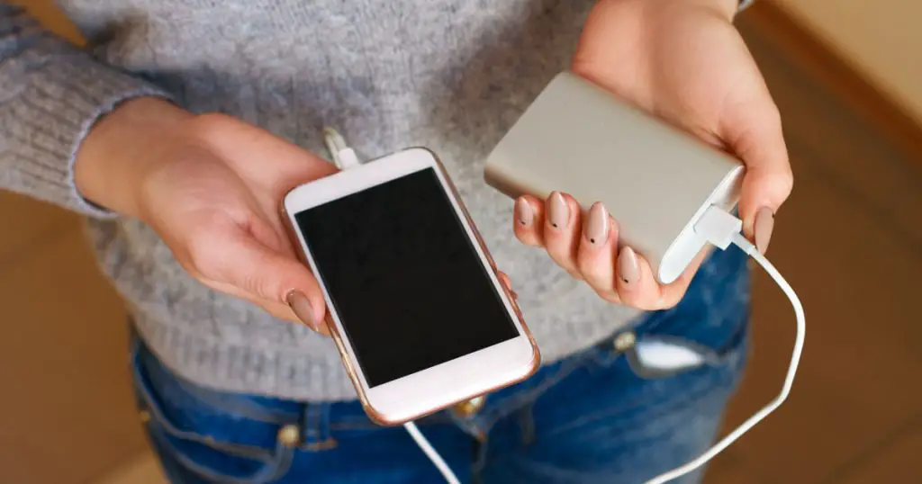 Two girls hands hold of the phone and charger. Powerbank and smartphone in girl's hands. Energy charger power bank smart phone. Still life modern digital concept.
