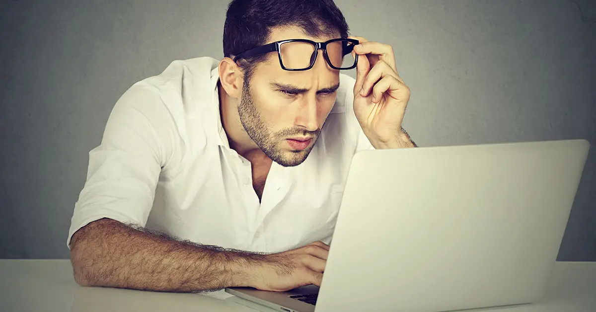 man lifting glasses to get focus more intently on what is displayed on laptop screen