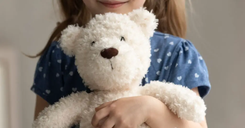 Close up of teddy bear in arms of child. Happy smiling little girl kid holding, hugging toy, playing with plush soft friend. Cropped portrait. Childhood, preschooler, playtime, childcare concep
