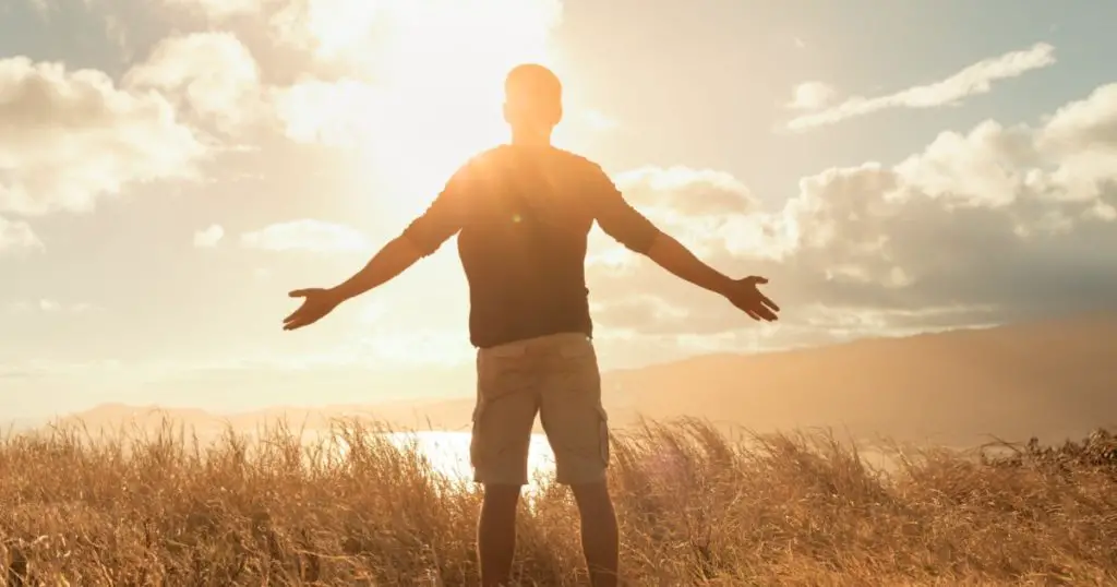 Young man feeing happy outdoors standing on a mountain taking in the warm rays of sunshine. Freedom, and happiness concept.