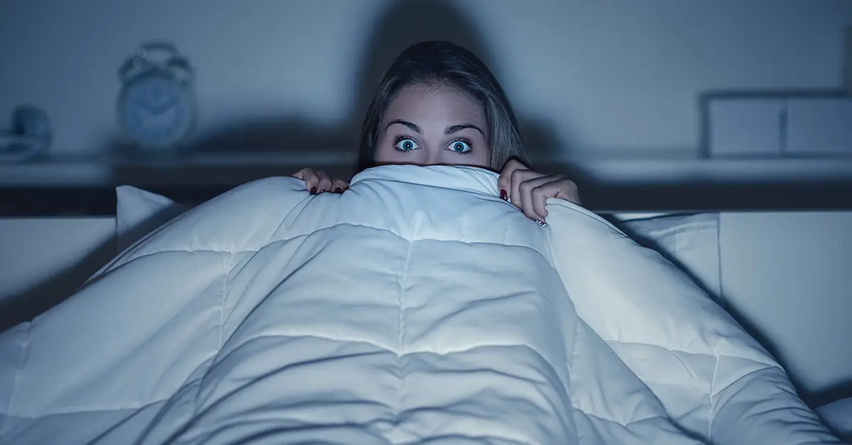 woman hiding under bed covers