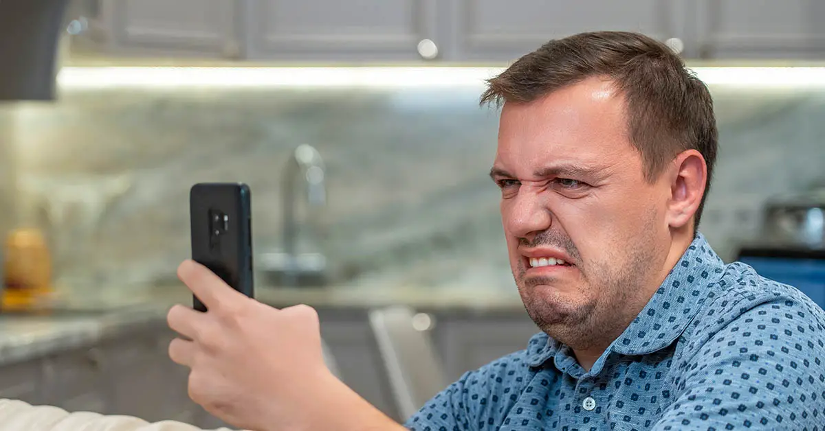 man cringing looking at smartphone