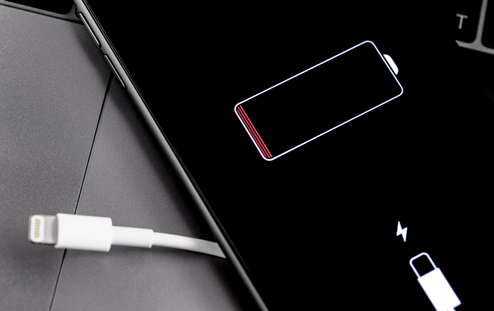 Apple iPhone smartphone with Lightning cable and battery logo on the display. Apple is a multinational technology company that designs, develops, online services. Moscow, Russia - July 12, 2019