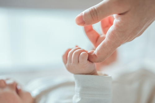 Close-up little hand of child baby holding hand of mother, A newborn holds on to mom's, dad's finger, Love and relationship with infant, Care and support, Dreaming and protection