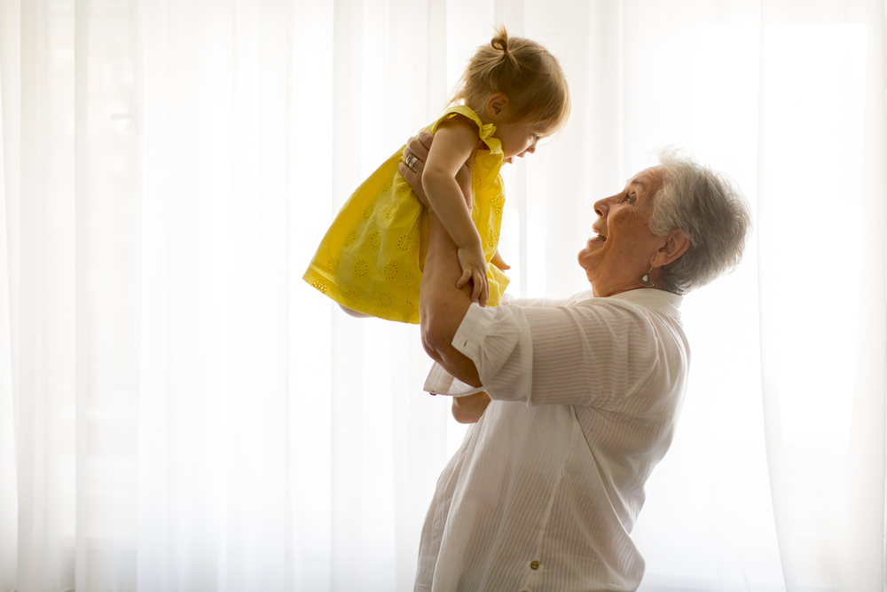 Grandmother holding little granddaughter in the room at home