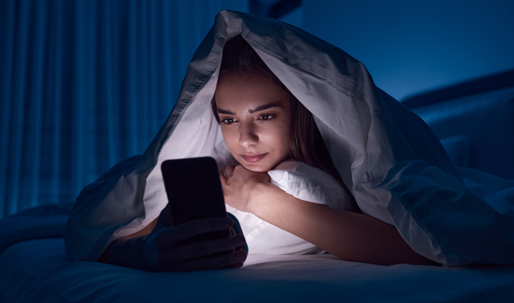 woman siitting on phone under bed cover